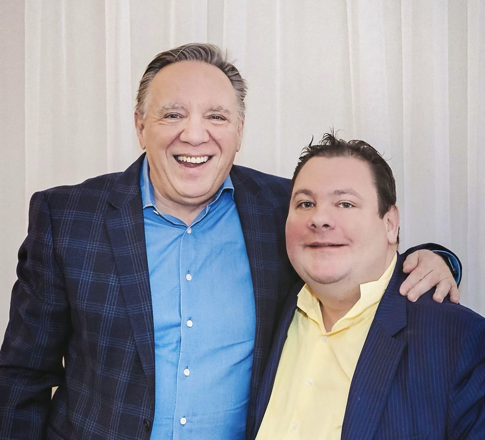 Deux hommes souriants posent côte à côte, l’un en chemise bleue, l’autre en chemise jaune.