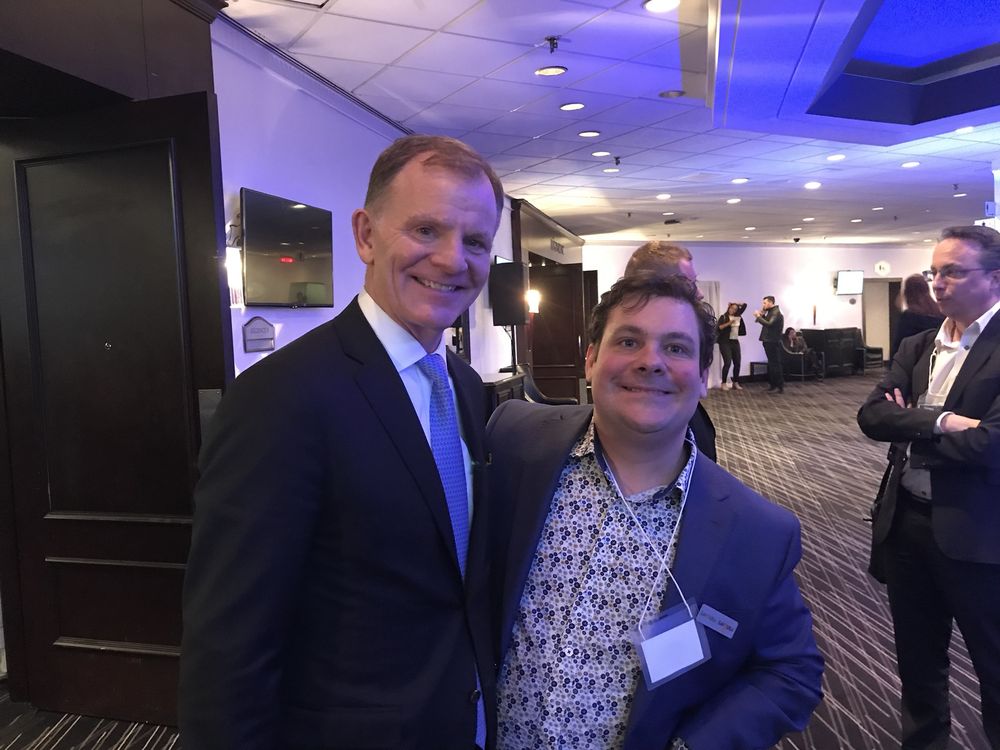 Deux hommes souriants posent côte à côte dans une salle de réception.