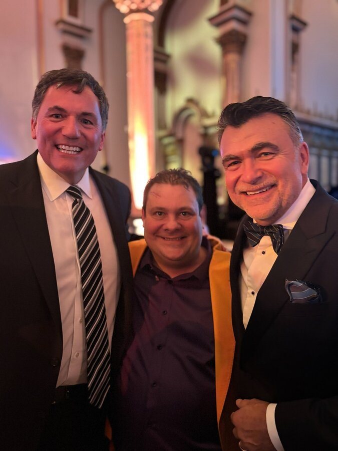 Trois hommes souriants posent ensemble lors d’un événement.